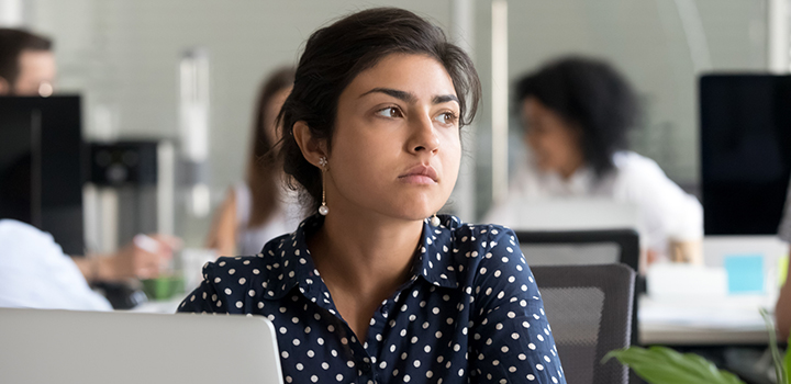 A woman in an office looks glumly away from her screen.