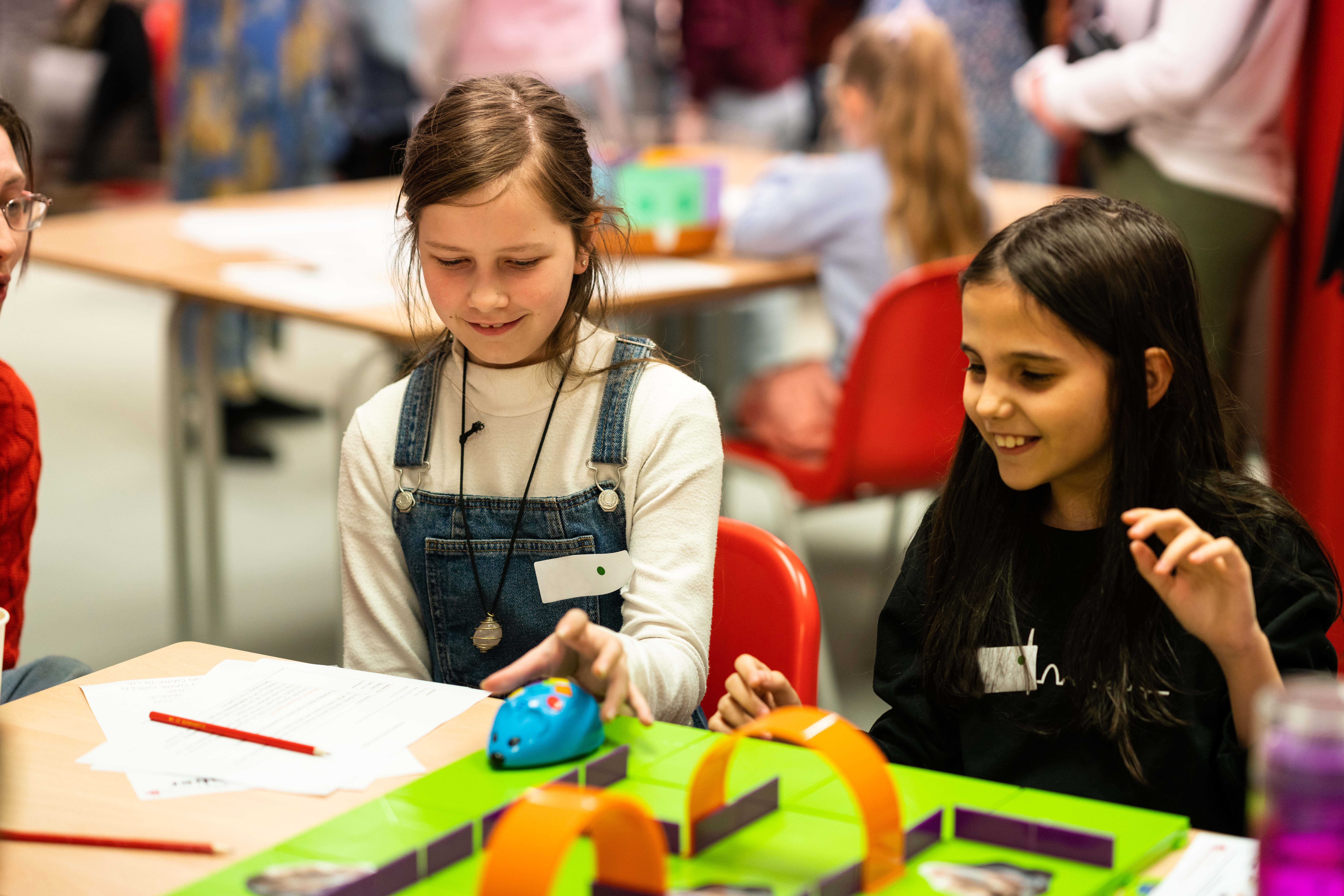 Two students smiling at a desk as they play a mouse game