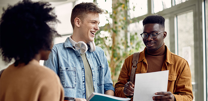 Three students smiling as they hold up exam result papers