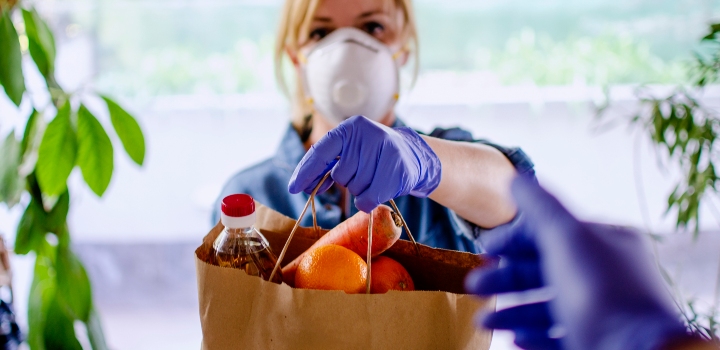 Volunteer in mask and gloves handing food to homeowner at their door